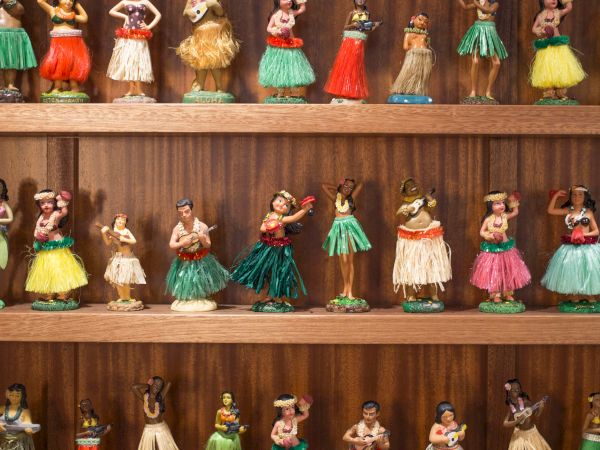 A collection of hula dancer figurines in colorful skirts is displayed on a wooden shelf, showcasing various poses and styles.
