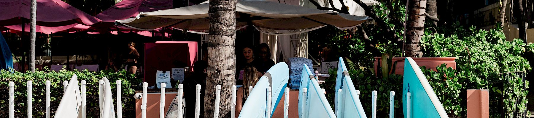 A resort sand play area with palm trees, umbrellas, and blue-and-white slide structures near a pool.