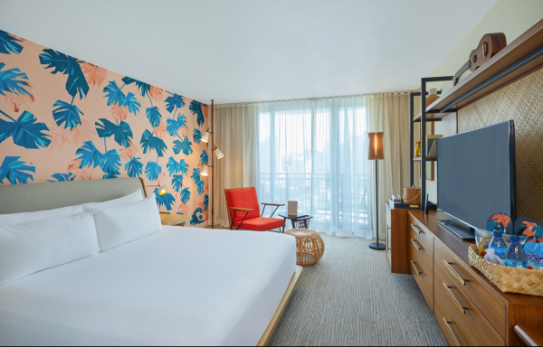 A hotel room with a tropical-themed wall, bed, red chair, wooden furniture, TV, and balcony.