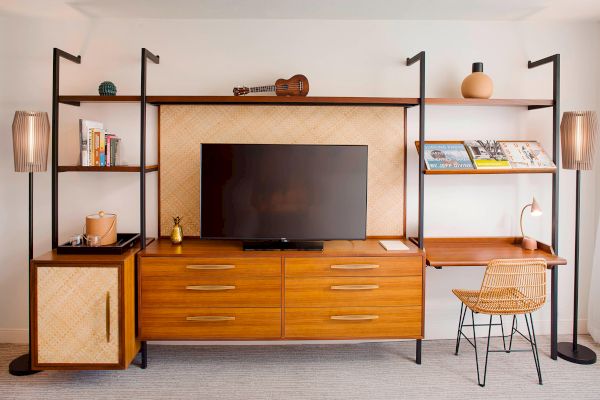 A modern wood media unit with a TV, shelves with books, decor, and work desk with chair, blending style and functionality.
