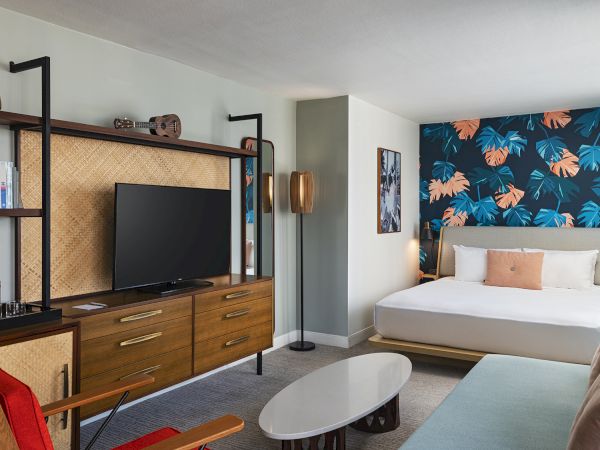 A stylish hotel-style living room with a bold blue botanical wallpapered accent wall, a flat-screen TV, modern furniture, and cozy seating.