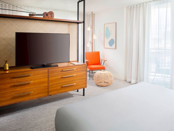 A modern hotel room with a wooden TV stand, an orange chair, and a bed. Light color scheme enhances spaciousness and elegance.