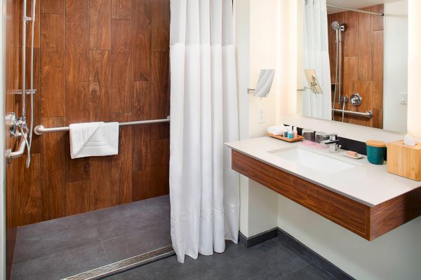 A modern bathroom with a wooden vanity, sink, large mirror, shower area, and white curtain.