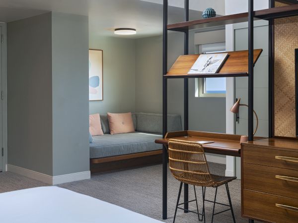 The image shows a modern room with a desk, chair, and shelves, and a seating area with two cushions in the background.