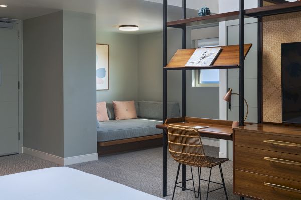 The image shows a modern room with a desk, chair, and shelves, and a seating area with two cushions in the background.