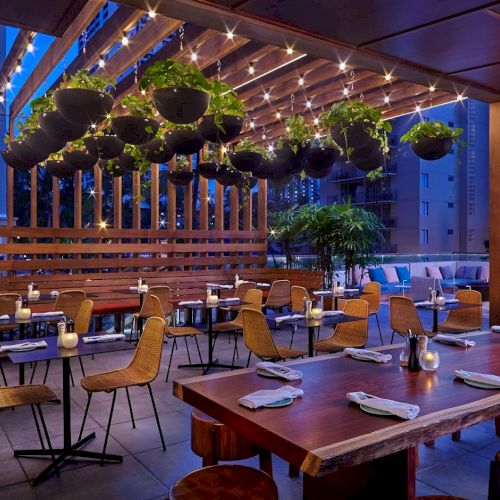 The image shows a cozy outdoor dining area with hanging plants, string lights, and modern tables and chairs set for a meal.