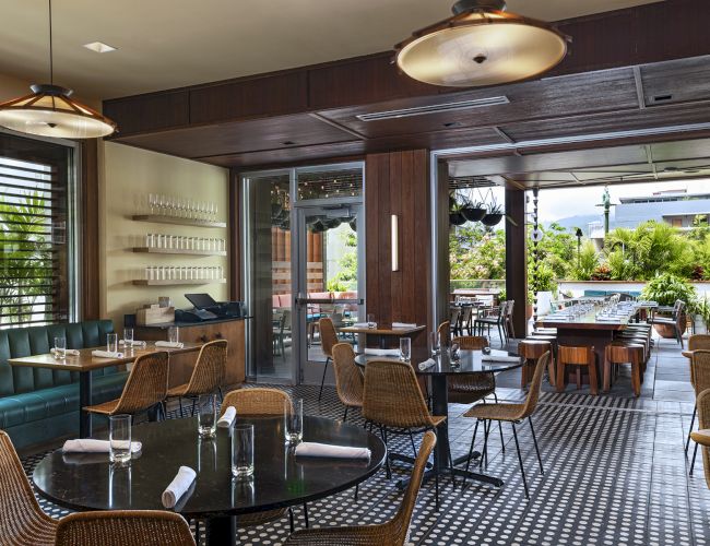 The image shows a modern restaurant with elegant seating, stylish lighting, and large windows overlooking green scenery.
