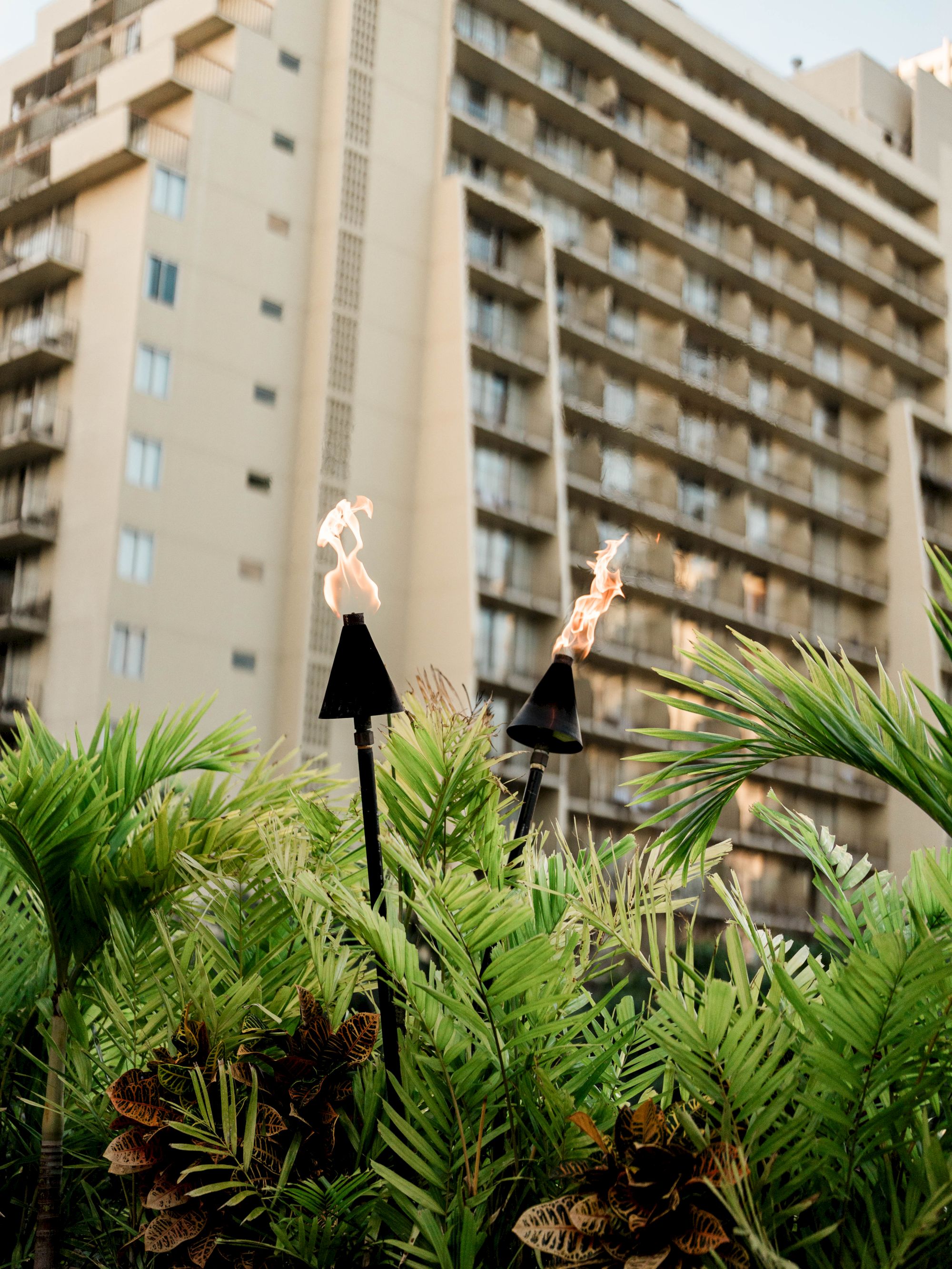 A landscaped courtyard with two flaming torches in front of a tall apartment/hotel building.