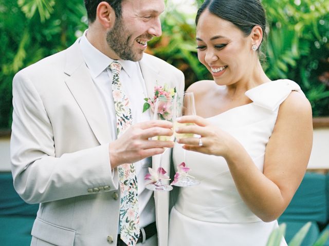 A couple toasting with drinks at a wedding or celebration, smiling in a garden setting.