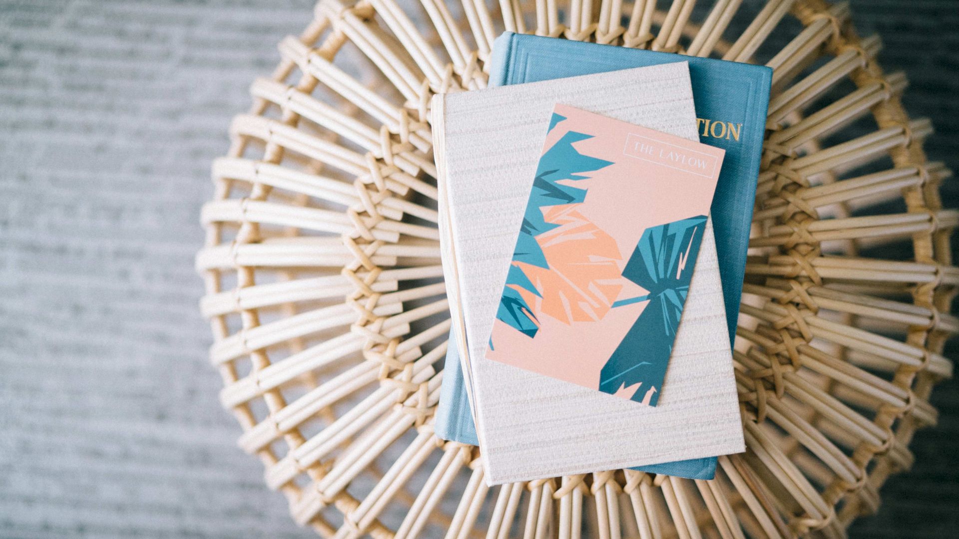 A wicker stool with a stack of books and a notebook featuring blue and pink leaf designs on top.