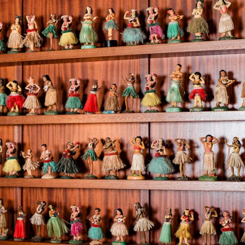 A shelf full of miniature dolls in colorful dresses, arranged in multiple rows, each with unique outfits and tiny features.
