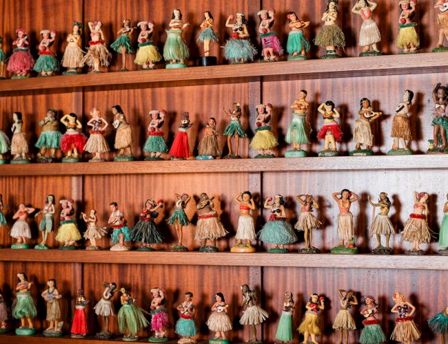 A shelf full of miniature dolls in colorful dresses, arranged in multiple rows, each with unique outfits and tiny features.
