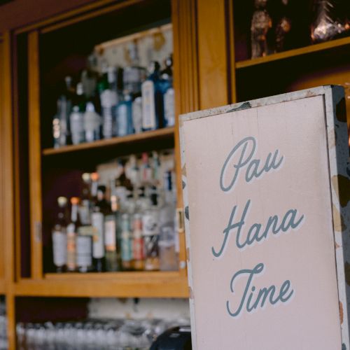 A bar with shelves of bottles, a handwritten sign on a whiteboard, and a bar counter in view. It's a cozy, dimly lit pub scene.