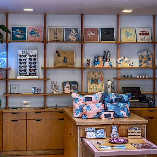 A cozy boutique with wooden shelves, colorful bags, tees, and a neon “OASIS” sign on the wall.