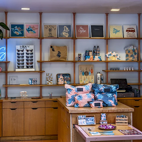 A cozy boutique with wooden shelves, colorful bags, tees, and a neon &ldquo;OASIS&rdquo; sign on the wall.