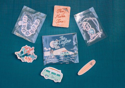 Assorted &ldquo;The Laylow&rdquo; Waikiki souvenirs&mdash;hula keychain, surfboard/van stickers, and &ldquo;Pay Hana Time&rdquo; card pieces.