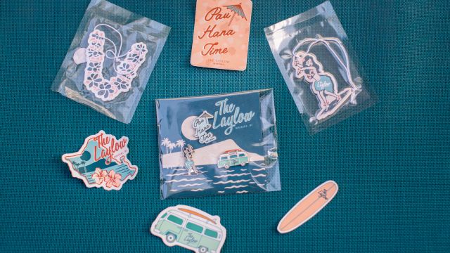 Assorted &ldquo;The Laylow&rdquo; Waikiki souvenirs&mdash;hula keychain, surfboard/van stickers, and &ldquo;Pay Hana Time&rdquo; card pieces.