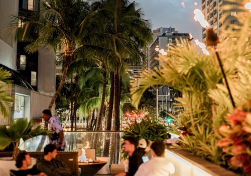A rooftop pool scene in the city with palm trees, lounge seating, and tall buildings at dusk, lighted tiki torches adding warmth.