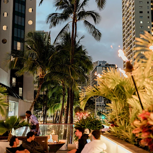 A rooftop pool scene in the city with palm trees, lounge seating, and tall buildings at dusk, lighted tiki torches adding warmth.