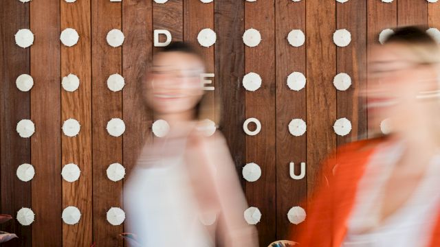 A rustic wooden wall covered with white pushpins and letter tiles as people walk by.