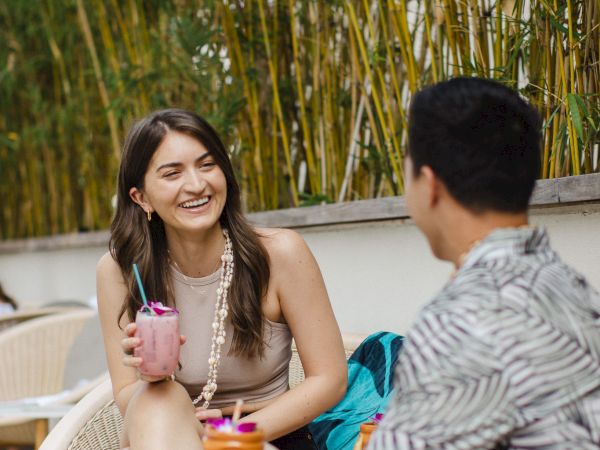 A couple relaxes on an outdoor patio by bamboo, smiling over colorful drinks.