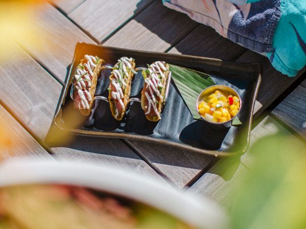 A black tray of topped appetizers with bean-sprout garnish and a small bowl of relish beside a folded branded towel.